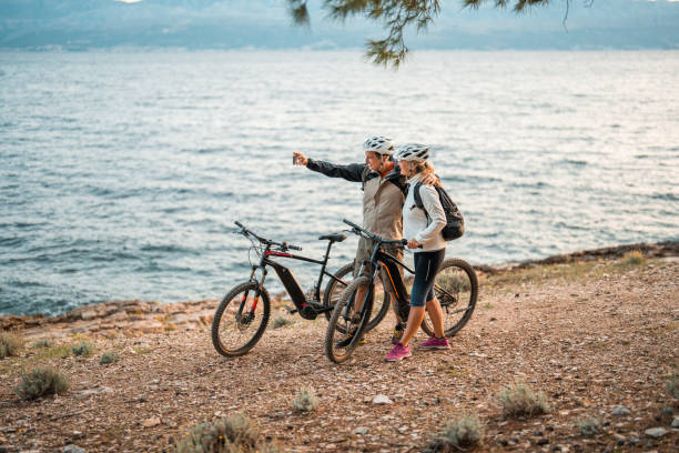 istock Active Senior Couple by Seaside with E-Bikes Taking Selfie at Dawn 2195462118