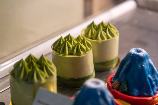 Colorful desserts are beautifully arranged, showcasing matcha-flavored treats with intricate peaks and a blue mountain dessert. The setting is a cozy sweets shop during the afternoon.