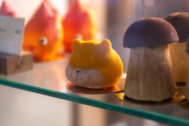Colorful and whimsical animal-shaped pastries are beautifully arranged in a bakery display case. A yellow cat-shaped treat stands out among other artistic confections.