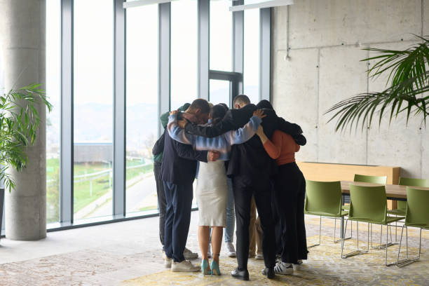 istock A diverse group of professionals standing in a supportive circle, embracing each other in a modern office space filled with natural light. 2195465288