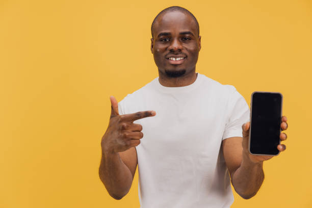 istock Young man pointing at smartphone with blank screen on yellow background 2195477265