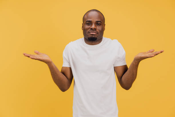 Puzzled african american man shrugging shoulders on yellow background