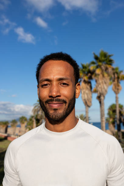 istock Young man smiling in front of palm trees and blue sky 2195478248