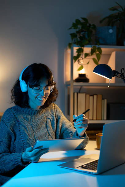 istock Young woman working from home at night using digital tablet and laptop 2195478354