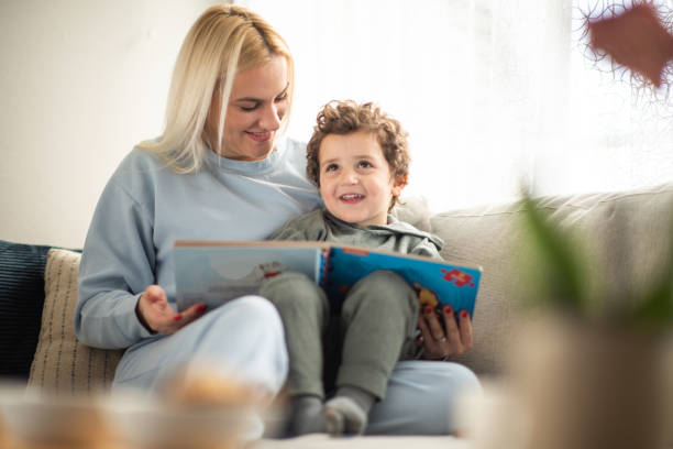 istock Mom and son sitting on sofa and reading book. 2195479437