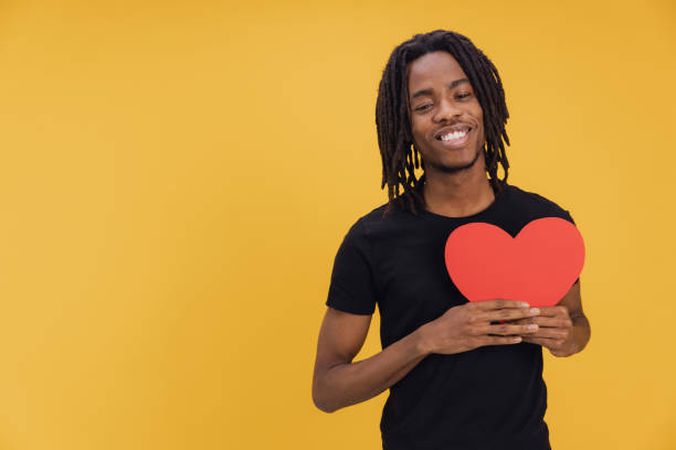 istock Young man holding a red heart on yellow background 2195480404