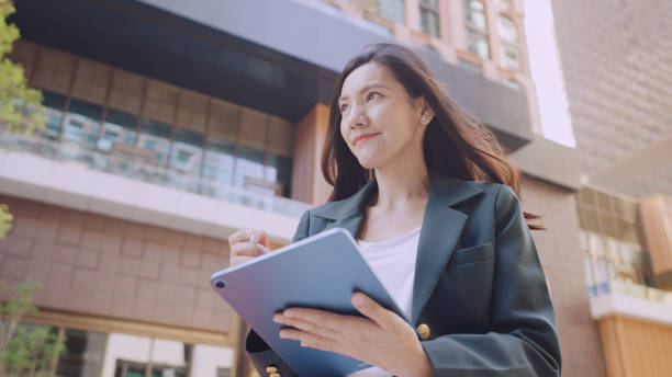 istock Confident businesswoman holding tablet outdoors in modern urban setting 2195482592