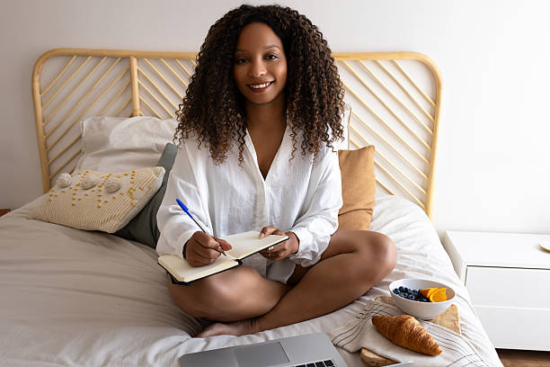 istock Young woman working from home sitting on bed taking notes in notebook 2195485025