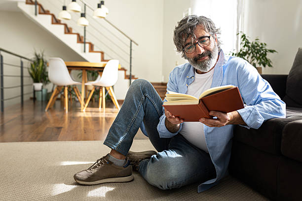 istock Senior man reading a book in his living room 2195485132