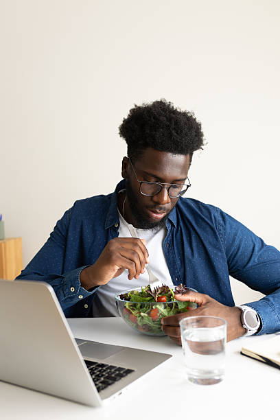 istock Young man eating salad while working on laptop at home office 2195485142