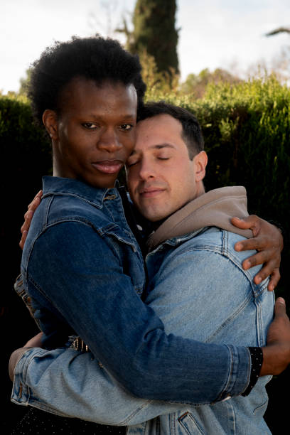 Two smiling men, a gay couple standing outdoors, sharing affection and forming a heart with their hands, urban romance and joy