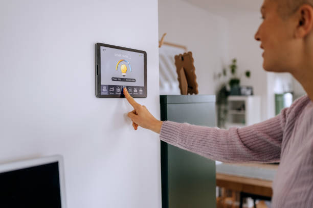 istock Casually clothed woman turning on light on smart home app on device attached on wall 2195487803