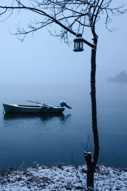 A serene winter scene featuring a snow-covered boat, a bare tree with a lantern