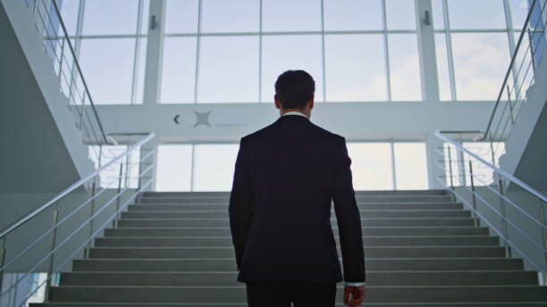 istock Determined businessman walking upstairs in light modern office back view. 2195490897