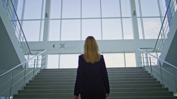 istock Confident businesswoman climbing stairs inside bright modern office building. 2195494496