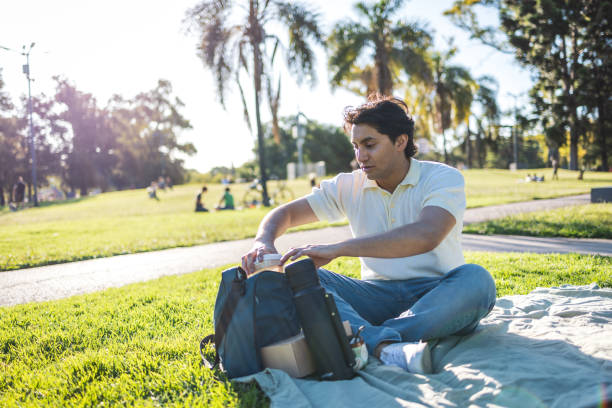 A young individual relaxes on a blanket at a sunny park, surrounded by vivid greenery and trees, capturing a serene and peaceful moment outdoors.