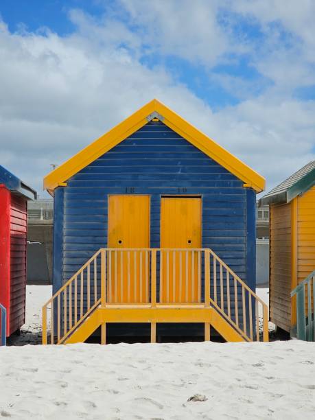 istock Colorful wooden beach huts standing side by side along sandy shoreline in muizenberg, cape town, with azure sky and scattered white clouds overhead 2195500321
