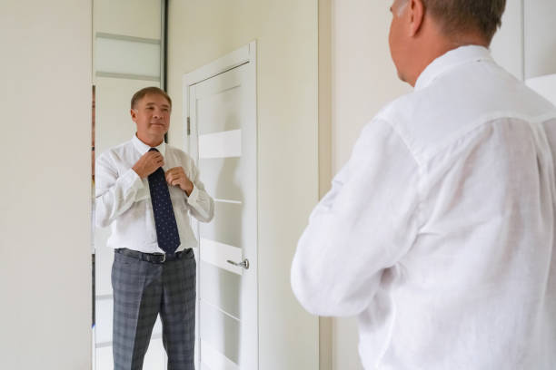 istock A man adjusting his tie in front of a mirror while preparing for an event in a well-lit room 2195501769
