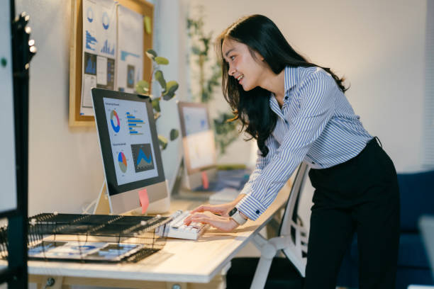 istock Professional businesswoman leaning over desk, carefully analyzing complex charts on computer screen, embodying workplace concentration and strategic planning in sleek office environment 2195503388