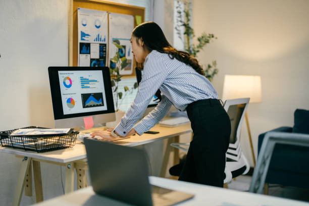 istock Professional businesswoman leaning over desk, analyzing charts and graphs on computer screen, representing concentrated work in modern office environment 2195503483