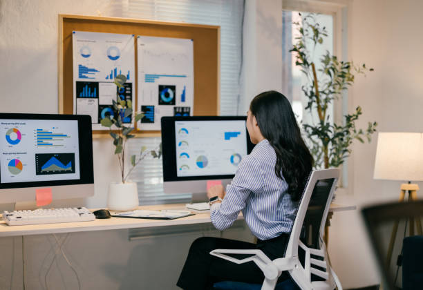 istock Businesswoman is sitting at her desk, analyzing charts and graphs on her computer screens in a modern office, focusing on data analysis and business performance 2195503681