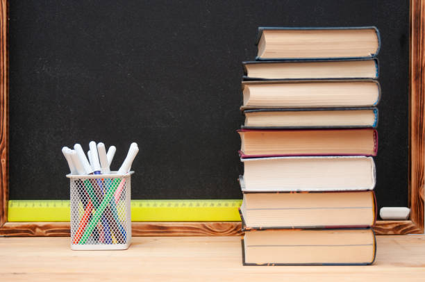 istock Stack of textbooks and felt-tip pens in pot in front of black chalkboard 2195507660