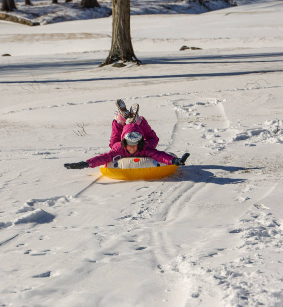 Happy child enjoying a fast ride on a red sled down a snowy hill in a winter forest, experiencing the joy of outdoor play