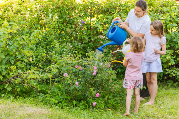 istock Mom teaching her daughters how to water plants 2195512097