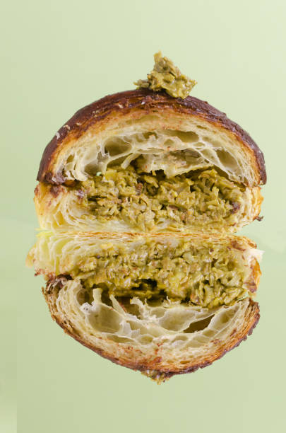 Croissant stuffed with pistachio paste and kadaif dough covered with dark chocolate on a gray plate in the cut . Unusual pastry with delicate filling. Trend food concept. Selective focus.