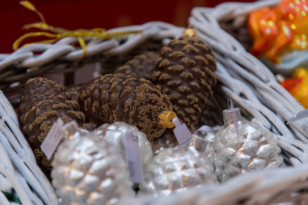 A basket filled with beautifully crafted holiday ornaments, including glittering pinecone shapes and shiny silver ornaments, showcased at a festive market setting.