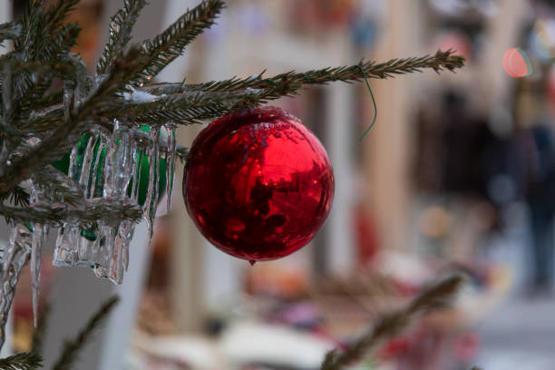 A vibrant red ornament dangles from a pine branch amidst a bustling winter market. Shimmering ice decorations complement the holiday atmosphere in December.