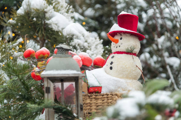 istock Snowman with red hat surrounded by snowy greenery and lantern in a winter wonderland setting 2195522888