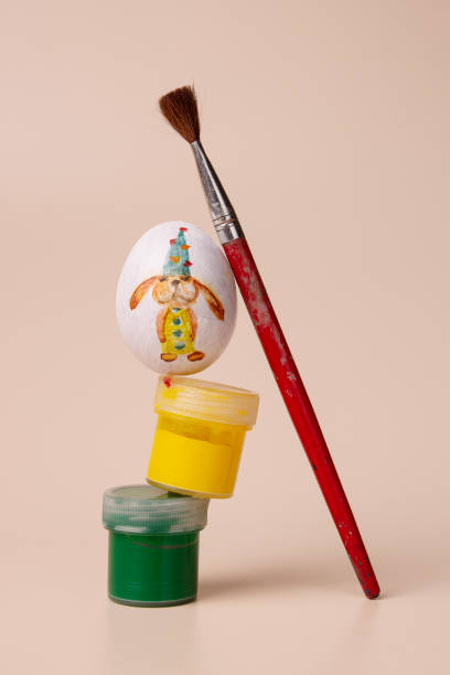 balance made from an egg with a rabbit pattern, jars of paint and brushes on a beige background