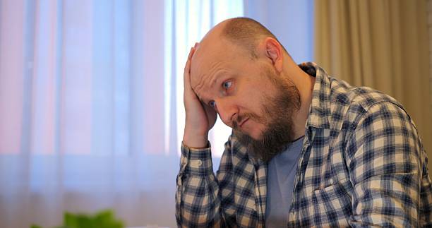 Bald man rubs forehead while stress builds in hectic workspace letting stress overshadow tasks if stress remains unchecked, warning viewers of potential burnout hazards. Remote work of man at computer