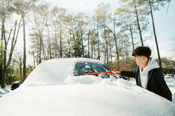 istock Teenage boy removing snow from car windshield with an ice scraper 2195532830