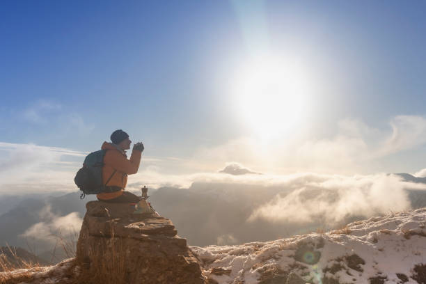 A mountain climber takes a moment to savor a coffee while sitting on a rock amidst snowy surroundings and vast, serene views