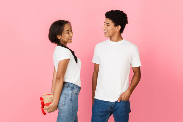istock Girl hiding present from boyfriend, pink background 2195534465