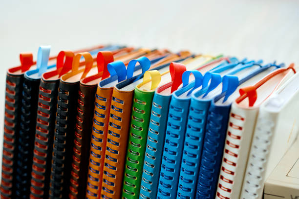 A vibrant row of leather spiral-bound notebooks in multiple colors, featuring decorative ribbons and a sleek modern design, perfect for stylish organization and writing..
