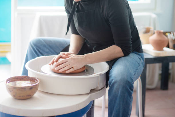istock Female hands throwing a large sized bowl on a potter's wheel in a sunlit pottery studio 2195548235