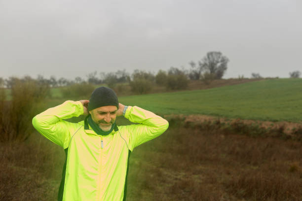 Madrid. Spain. Mature man wearing fluorescent jacket adjusting his beanie before running in a cold and foggy winter day in the countryside