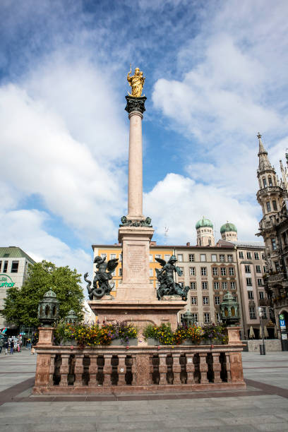 Munich, Germany - view of the clock towers  of the Frauenkirche, Munich cathedral, a pinnacle of the gothic New Town Hall and in the foreground the golden statue of the Holy Mary (Mariensaeule) in Marienplatz