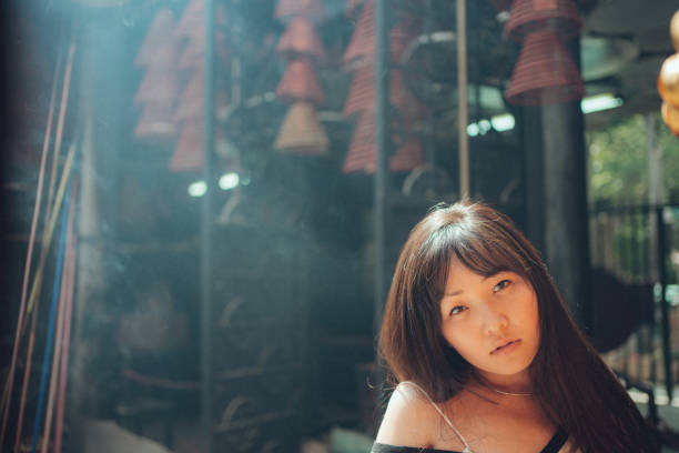 A woman stands in a temple setting, surrounded by incense smoke and soft sunlight filtering through.