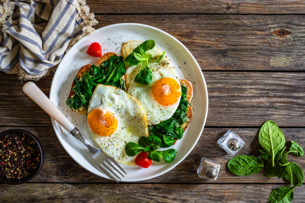 istock Crispy toast with stewed spinach and fried eggs with runny yolks on wooden table 2195570478