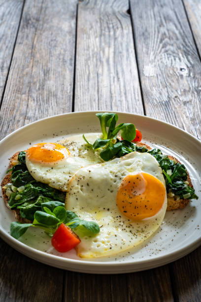 istock Crispy toast with stewed spinach and fried eggs with runny yolks on wooden table 2195570512
