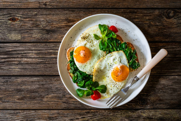 istock Crispy toast with stewed spinach and fried eggs with runny yolks on wooden table 2195570594