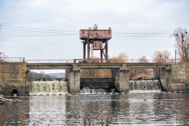 Historic hydroelectric dam situated in a rural landscape, surrounded by water and natural vegetation. Soft natural light highlights the textures of the structure and the serene countryside setting.