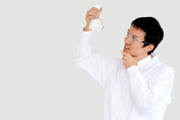 A young Asian male scientist in a white coat is looking at a flask