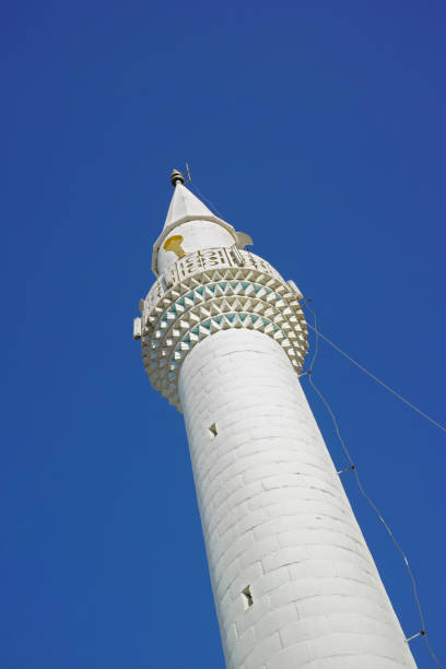 A tall, elegant white minaret stands against a vibrant blue sky, showcasing architectural beauty and cultural significance with its slender design and intricate details.