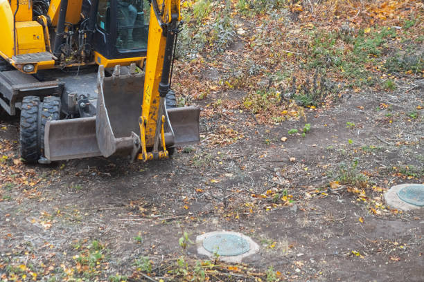istock A yellow excavator stands on a site with fallen leaves and visible manholes. 2195589348