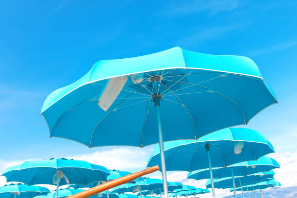 A minimalistic close-up of two large outdoor umbrellas, one green and one red, commonly used in open-air cafes, patios, and hotel terraces. The fabric structures stand out vividly against the cloudless blue sky, capturing the essence of summer shade, hospitality, and relaxed social settings.